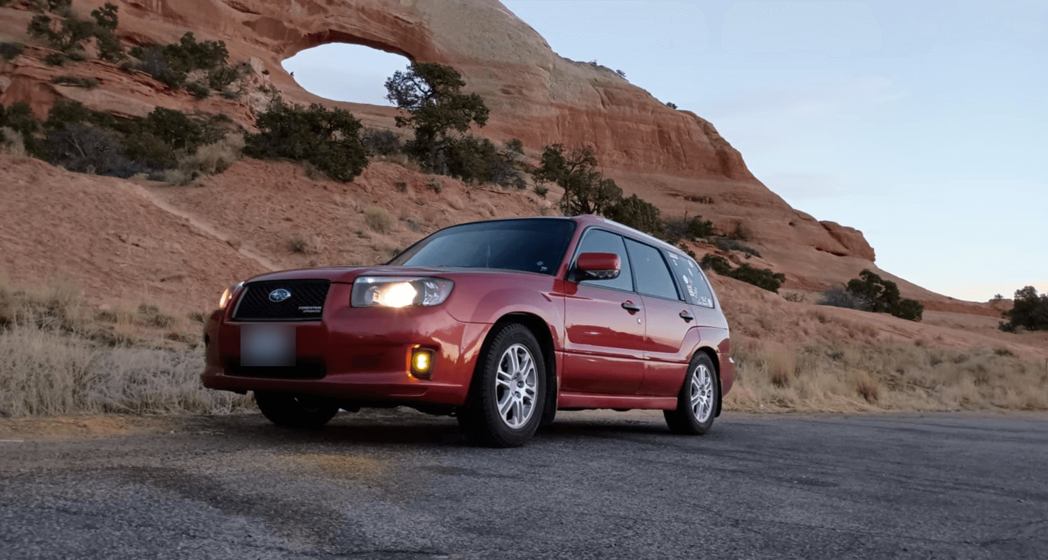 Red Subaru Forester Sports with SMITHtRONiC amber fog lights parked below a desert rock arch