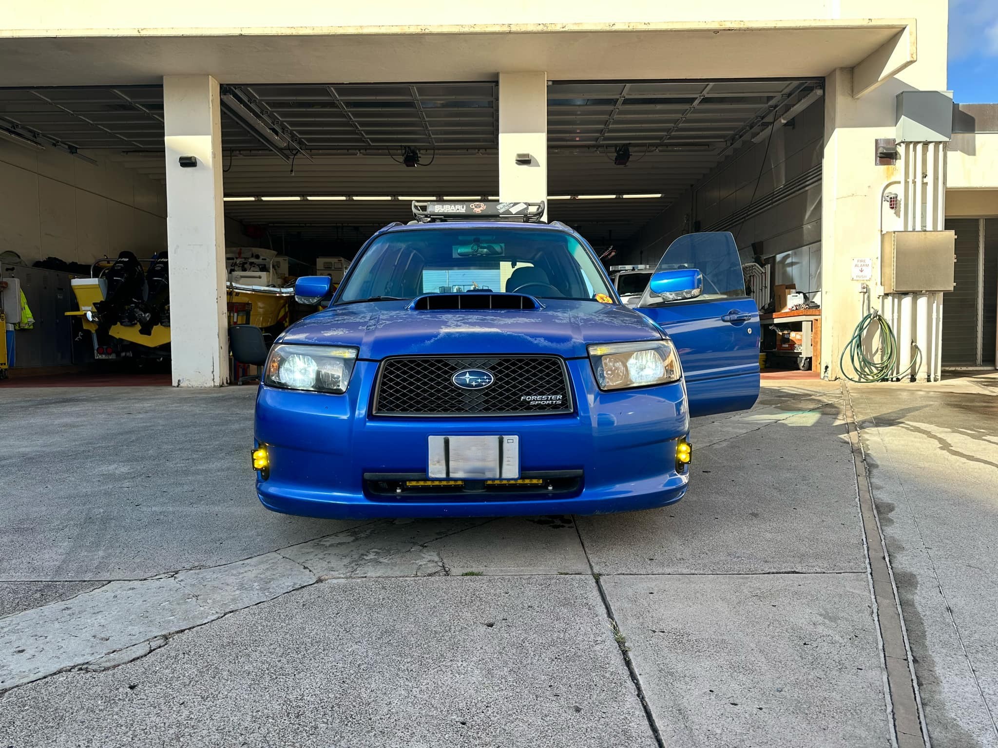 Blue Subaru Forester Sports head-on in a garage bay with amber fog lights lit