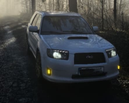 White Forester head-on in the fog with amber fog lights and headlights on